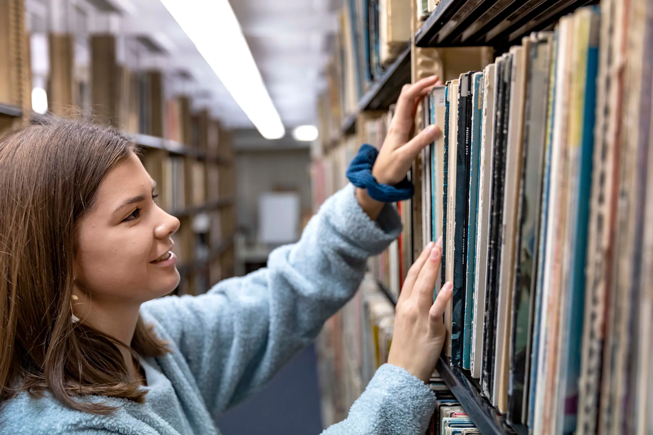 Student selecting a book from library shelves